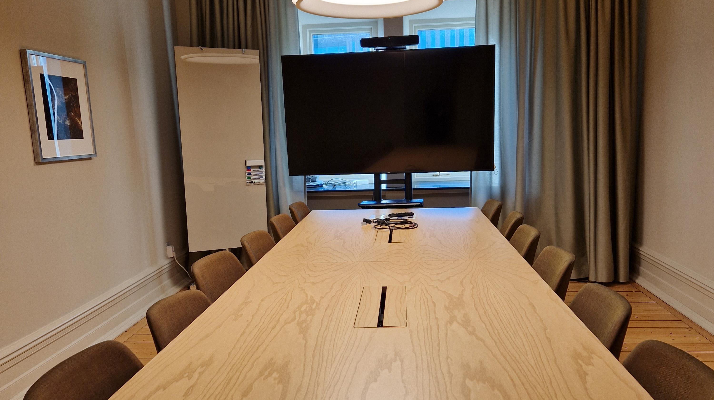 Avlångt konferensbord och bildskärm på kortsidan av bordet.