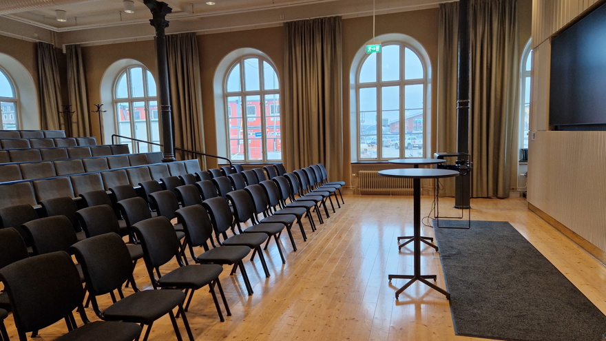 Stolar i biosittning, bildskärm samt två ståbord.