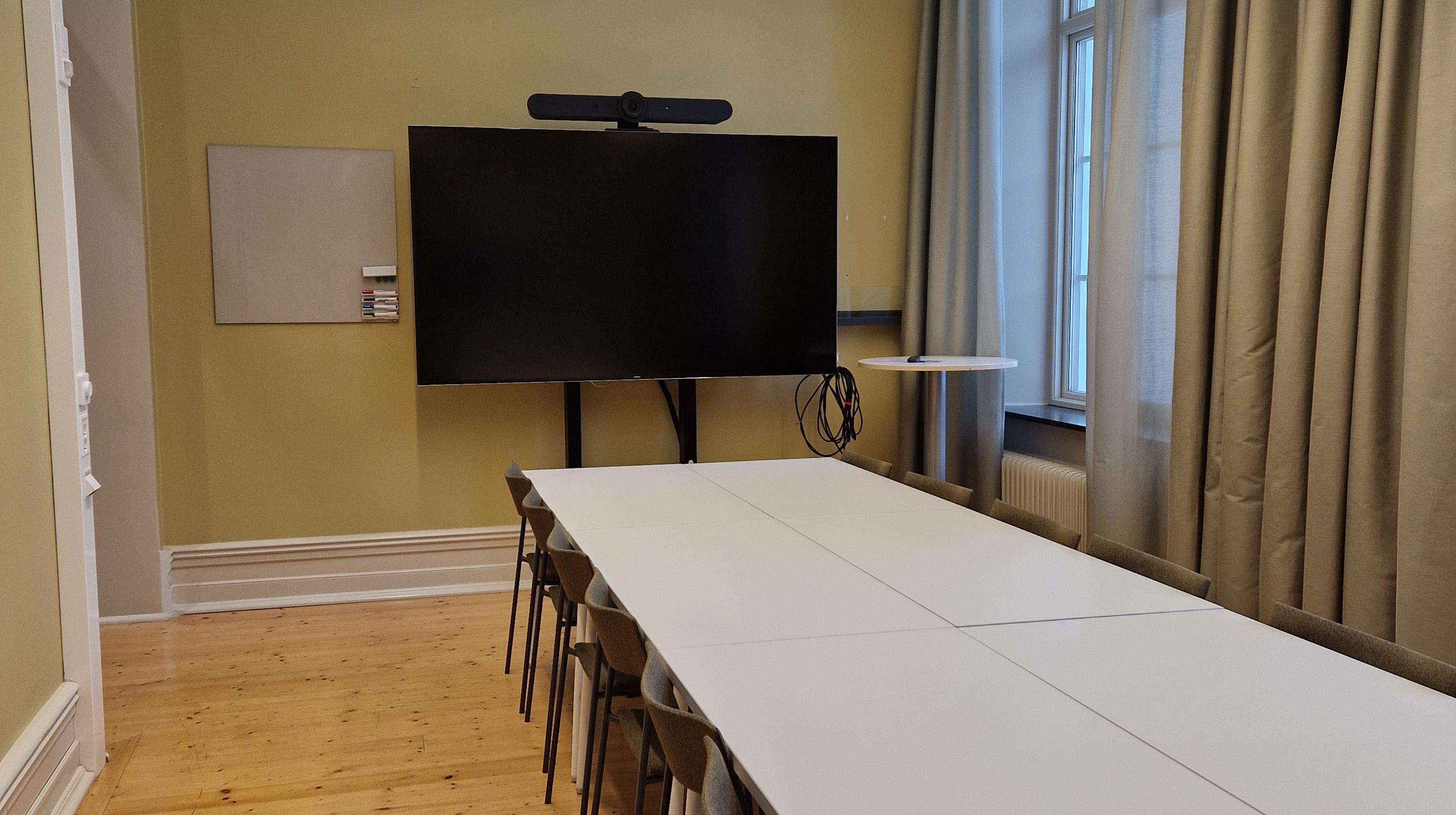 Avlångt bord samt tv-skärm vid kortsidan av bordet.